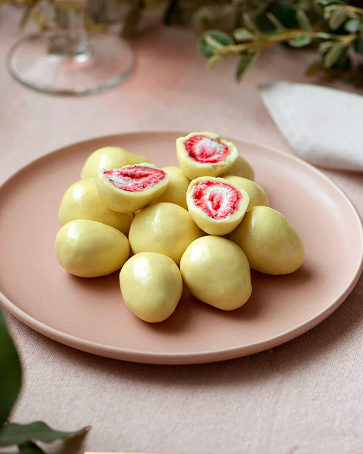 Freeze dried strawberries in white chocolate presented on a pale pink plate.