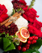 Close-up of Eve Christmas floral arrangement showing orange ornaments, roses & cinnamon sticks