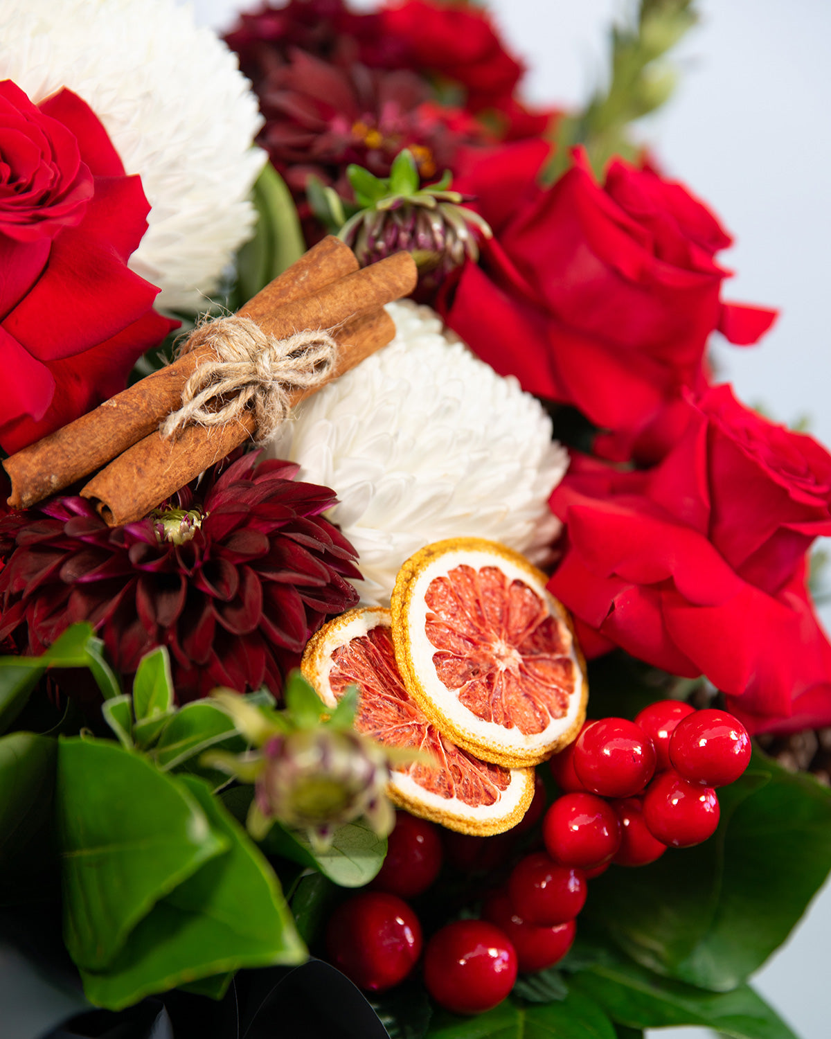 Close-up of Eve Christmas floral arrangement showing orange ornaments, roses & cinnamon sticks