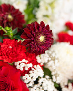 Close-up of luxury Christmas flower arrangement with red roses, dahlia, white disbuds, and seasonal greenery