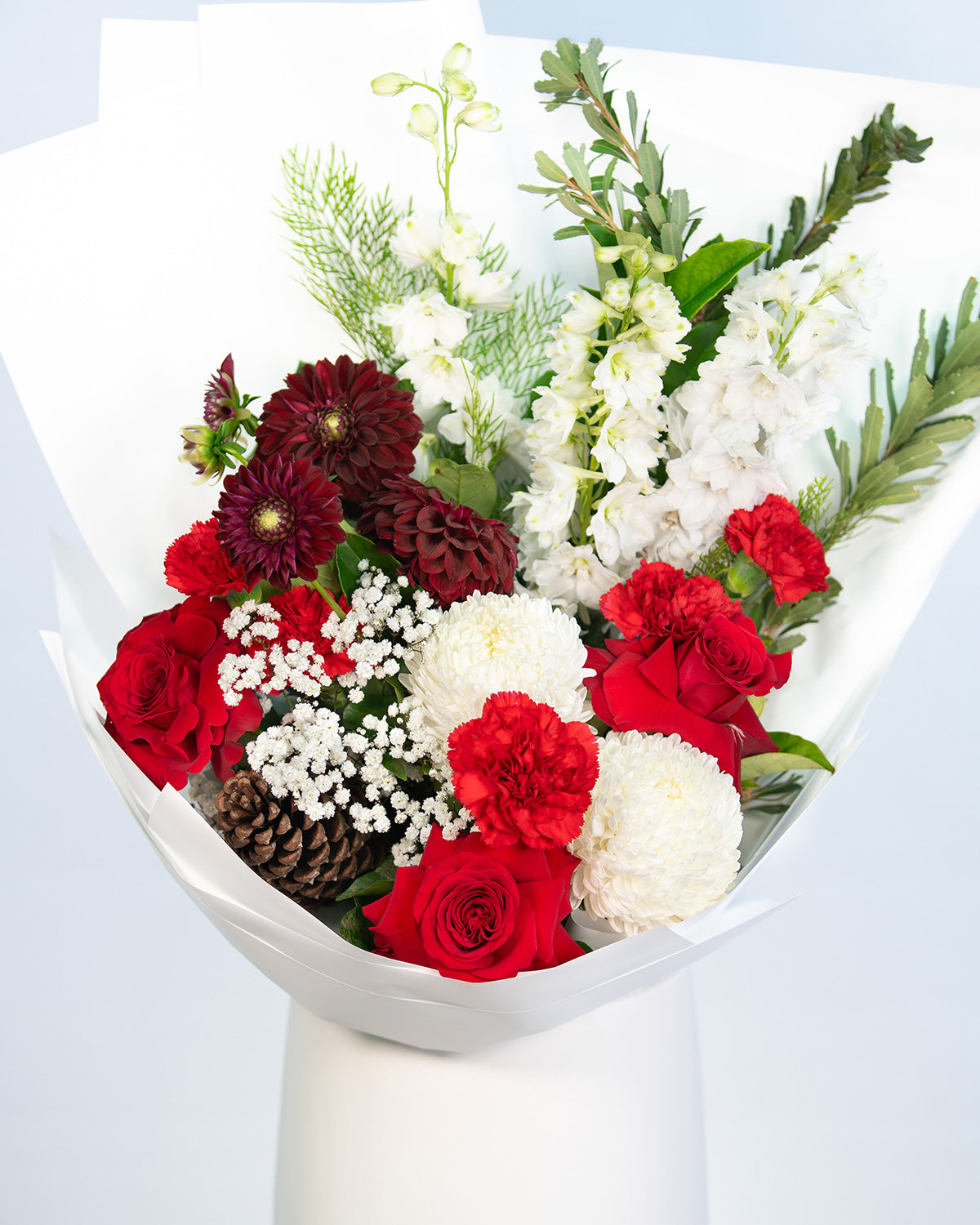 Holly Christmas bouquet featuring red roses, white blooms, and festive pine cones arranged by Brisbane Market Flowers