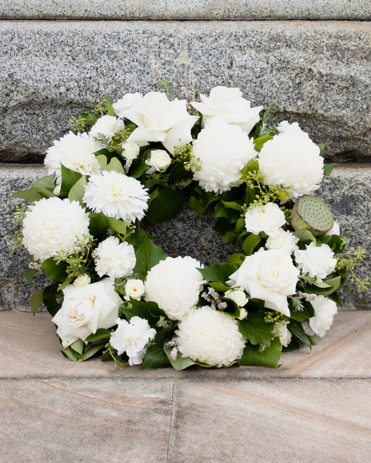 A wreath of white chrysanthemums, roses and other seasonal flowers with green leaves, arranged on a grey stone  Anzac display.