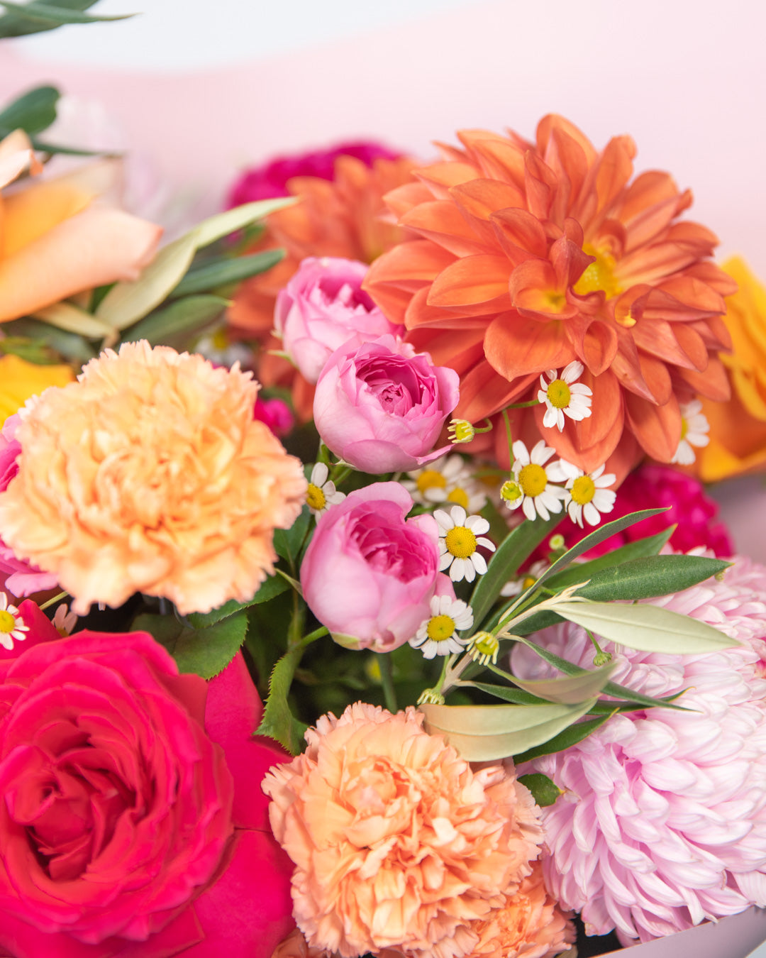 Close up of bright summer flowers including chamomile, carnations and dahlia in orange and pink tones.